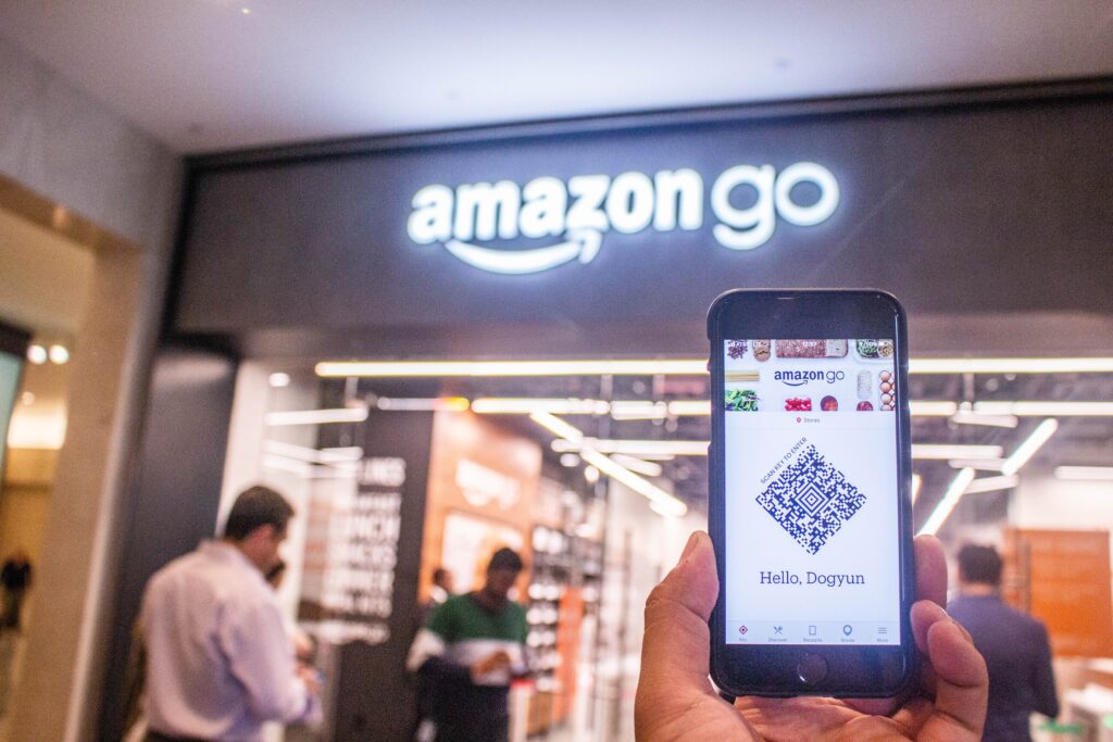 Mâna ținând un telefon în afara magazinului Amazon Go