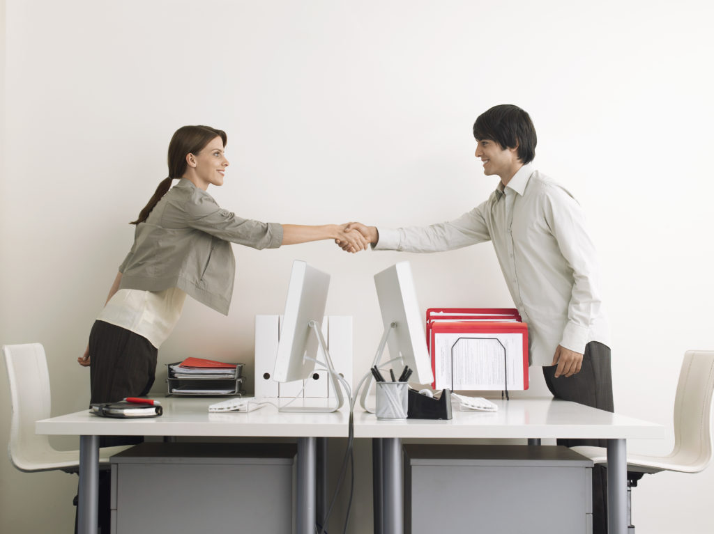 two people shaking hands over a desk