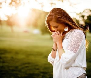 woman bowing her head in prayer outside 