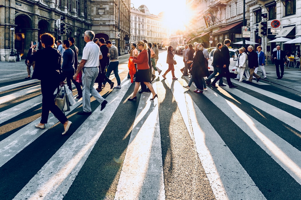 crowd of people walking across the street at sunset 