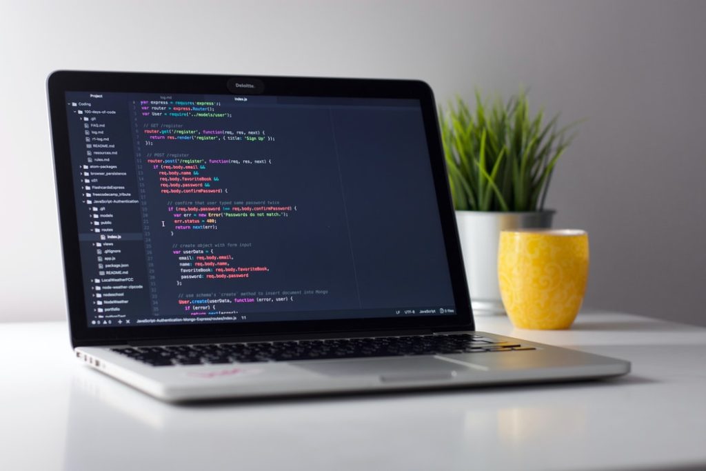 code on a laptop screen on a white desk with plant and yellow cup