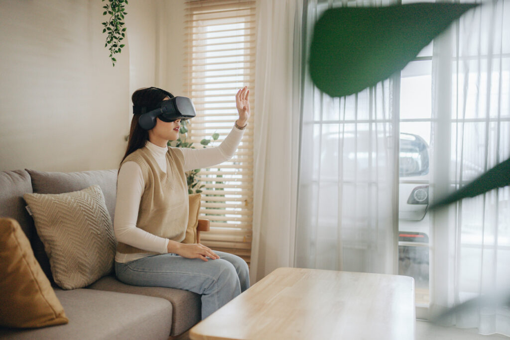 メタバース: リビング ルームで VR メガネをかけて仮想市場で買い物をする若い女性。