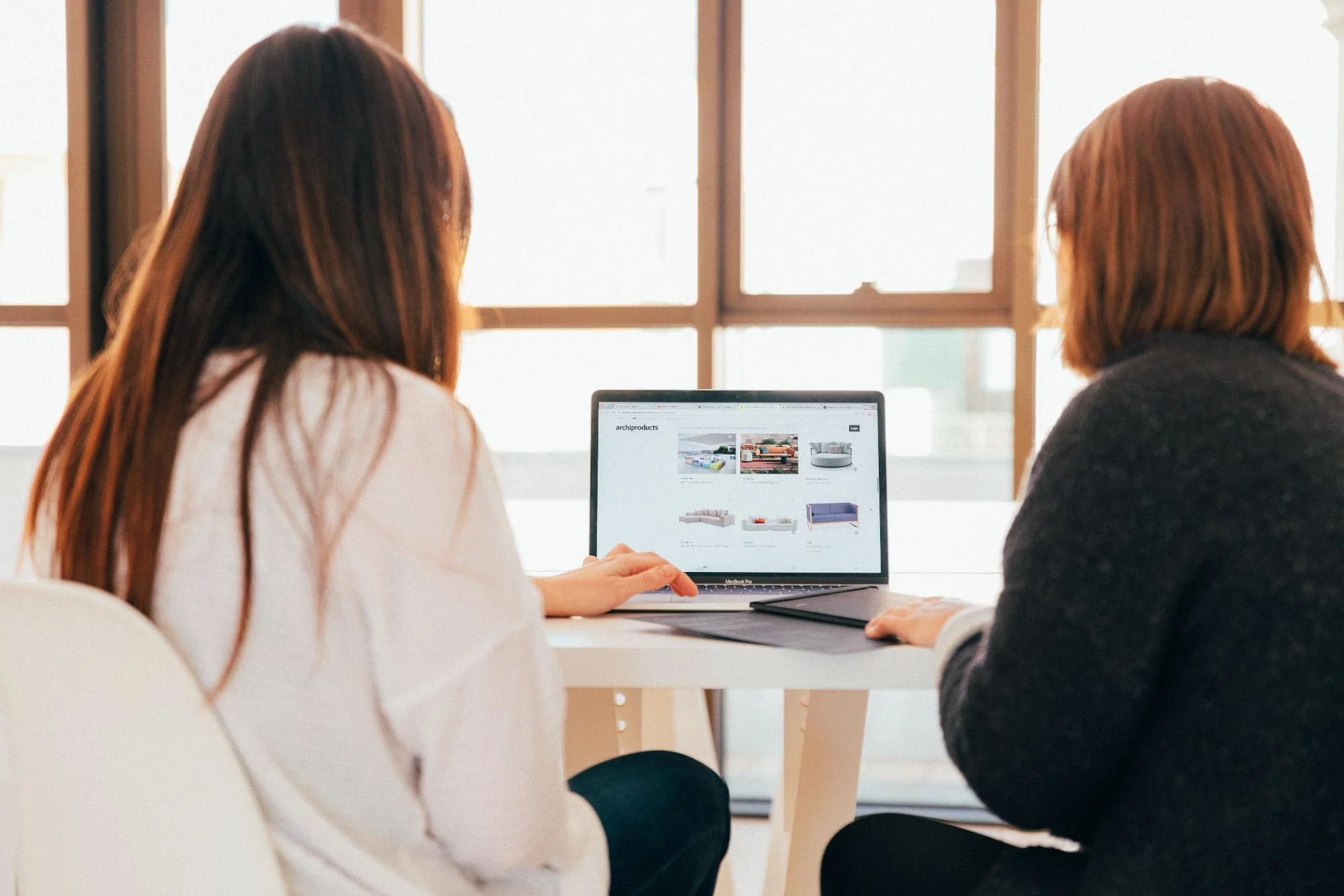 Duas mulheres caucasianas sentadas lado a lado com um laptop no meio, passando pela jornada do cliente