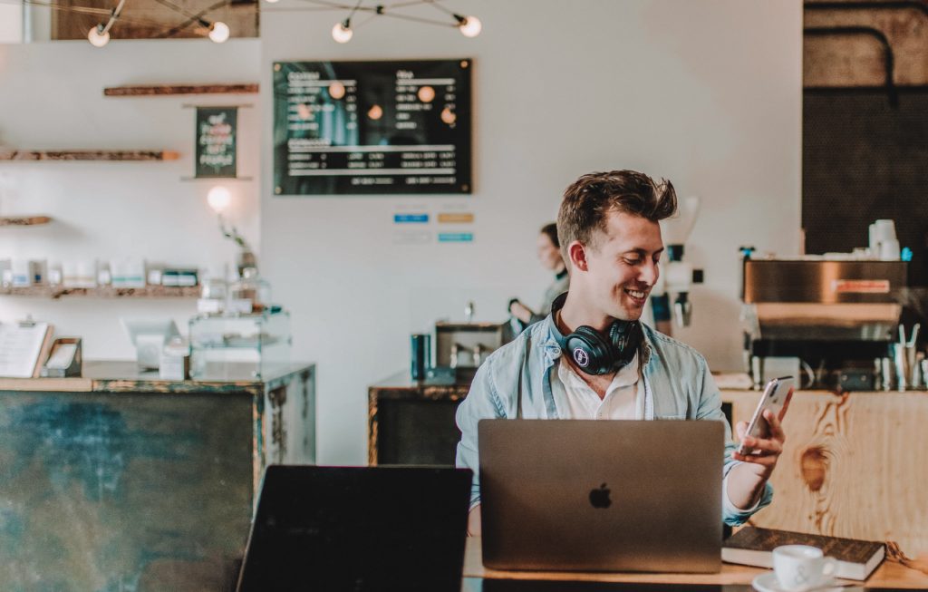 Homem usando smartphone e Mac Book e sorrindo