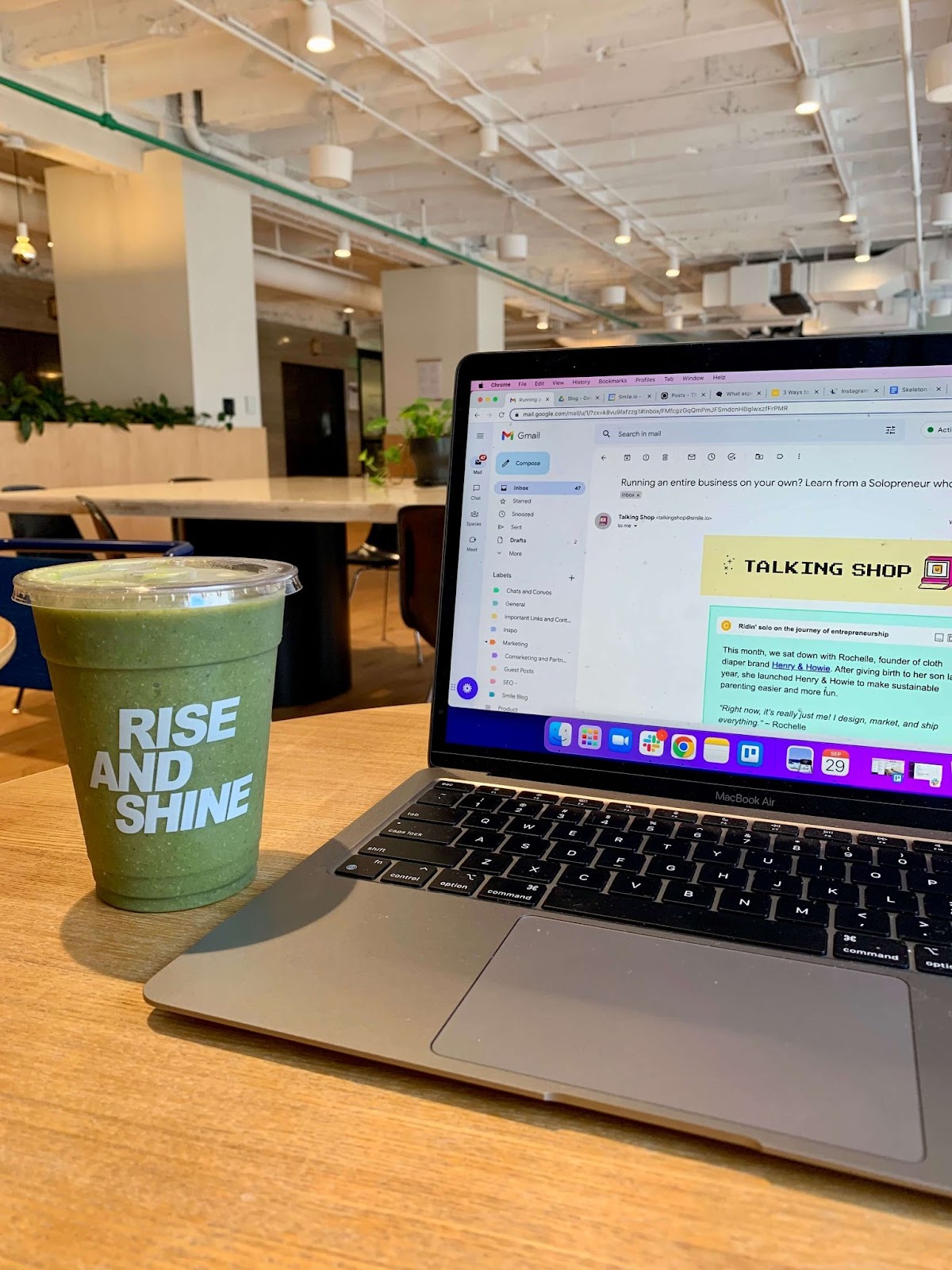 Talking Shop Smile Newsletter–Gambar MacBook di atas meja kayu terbuka untuk buletin Talking Shop, yang merupakan buletin gaya 8-bit dengan warna-warna cerah. Ada smoothie hijau di sebelah laptop dalam cangkir bening bertuliskan, "Bangkit dan Bersinar".