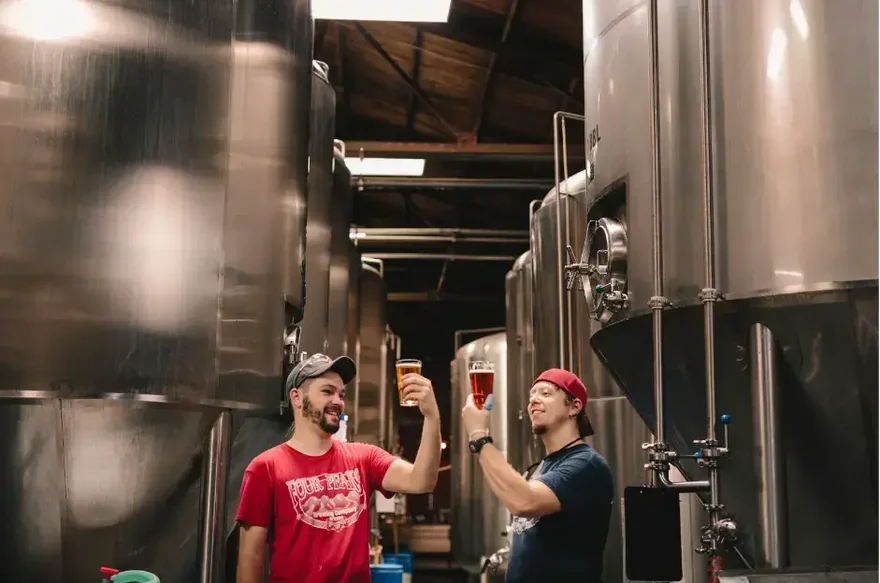 dois homens provando cerveja perto de tanques cilíndricos