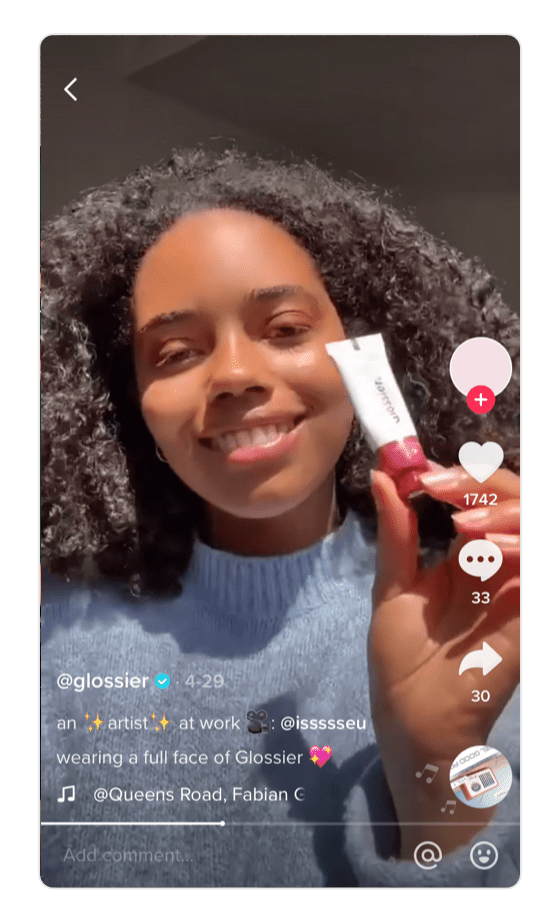 Screenshot di TikTok di Glossier. La donna tiene il prodotto davanti alla fotocamera e sorride.